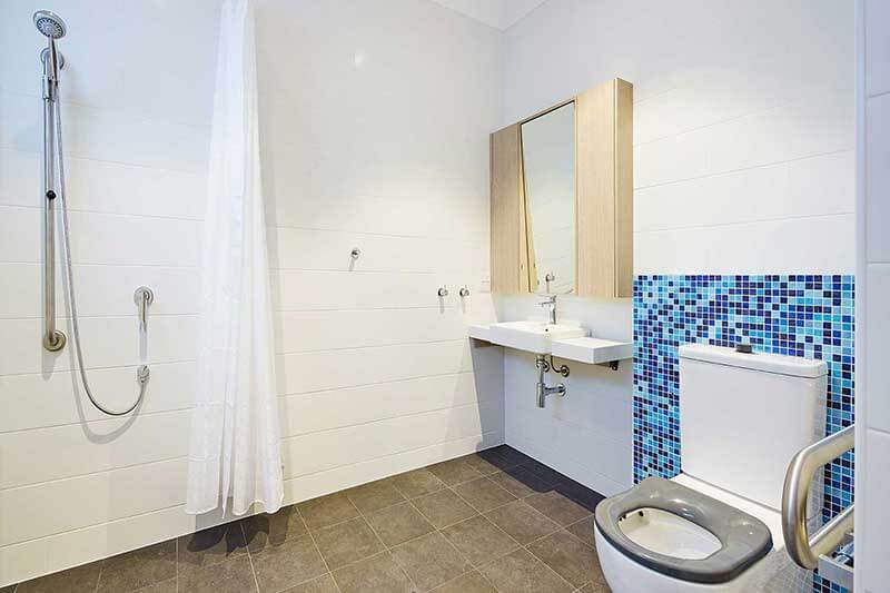 Accessible bathroom with shower, toilet and sink. White tiles with handrails and mosaic feature